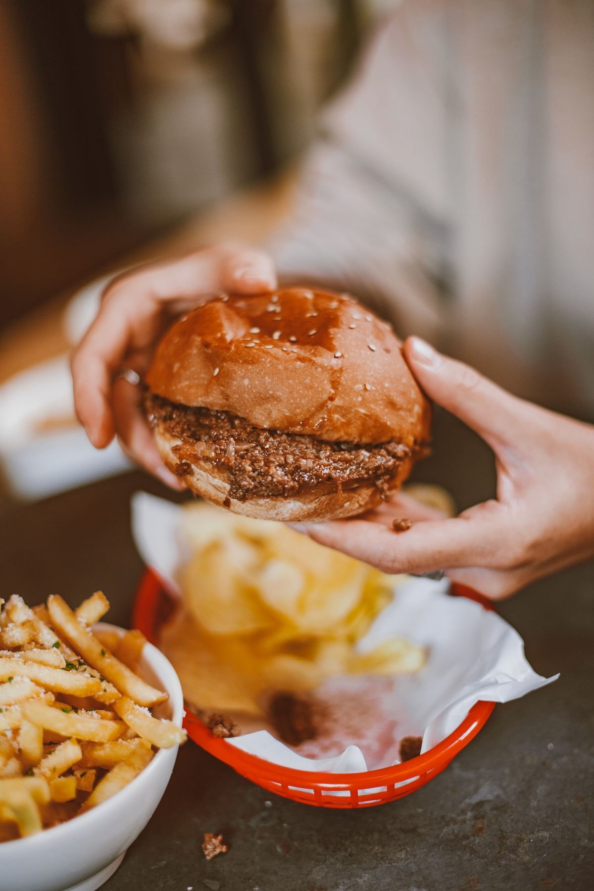 Two hands holding a beef burger beside a serving of fries, used as an editorial illustration for “McGangBang: a fan mash-up, politely ordered”