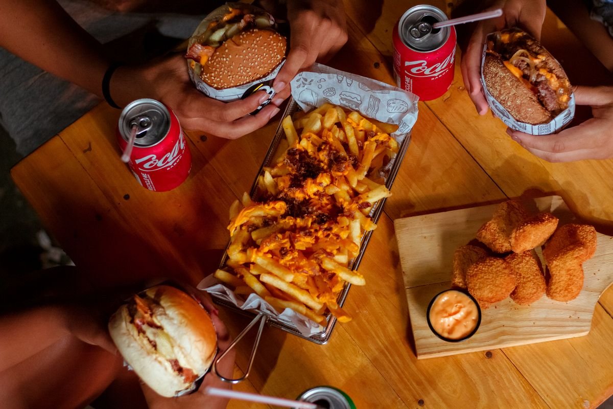 A wooden table with burgers, fries, chicken nuggets and drinks